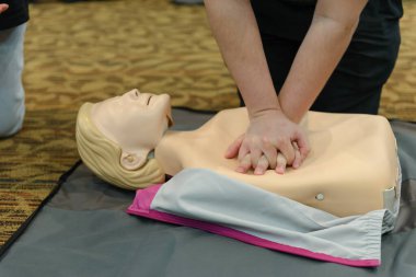 CPR First Aid Training with CPR dummy in the class. Demonstrating chest compressions concept