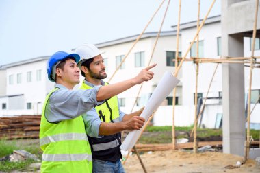 İnşaat mühendisi ve mimar kontrol planı inşaat alanının planıyla çalışıyor. Güvenlik için kasklı güvenlik yelekleri giyiyorlar. İnşaat projesi kavramı