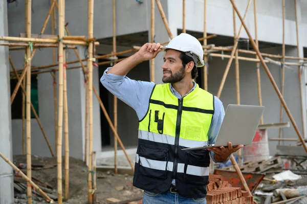 年轻迷人的建筑 身穿白盔背心 手持笔记本电脑 站在建筑工地上 笑容满面 住房建设项目 — 图库照片