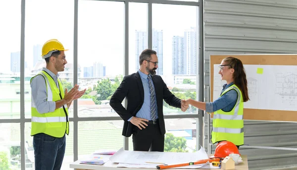 construction manager and engineer construction woman in protective uniform shaking hands while working finish an agreement in the office construction site, Successful deal concept