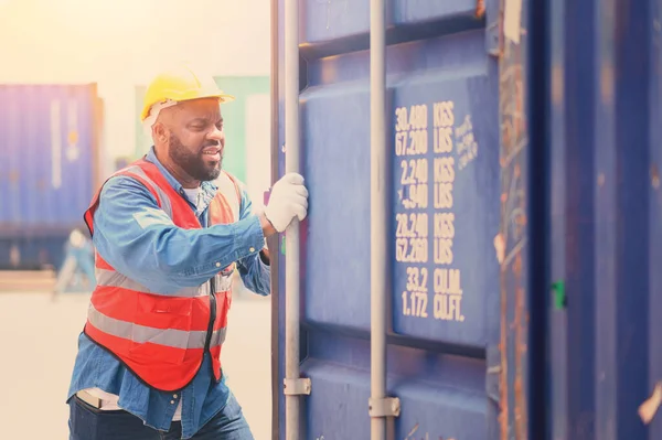 African American logistic workers wear yellow helmets and reflection shirts and open containers for inspection and check the condition of containers at warehouse container yard. logistics business import export industry