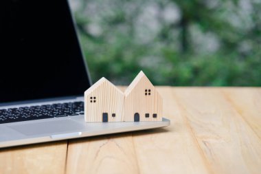 Loan real estate or property mortgage investment concept. House wooden model with computer laptop on wooden table with copy space.