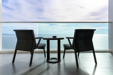 Mavi gökyüzünün altında deniz manzaralı kül tablası ve iki modern rattan koltuk. Seyahat balkonundan manzara. Yaz tatili kavramı. tatil yeri