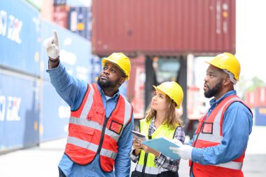 Profesyonel konteynır operatörlerinden oluşan bir grup kadın ve erkek konteyner deposunda kameraya bakın ve onaylayın. Lojistik personel konteyner kargo alanlarında çalışıyor ve endüstriyel konteynır kargolarını kontrol ediyor.