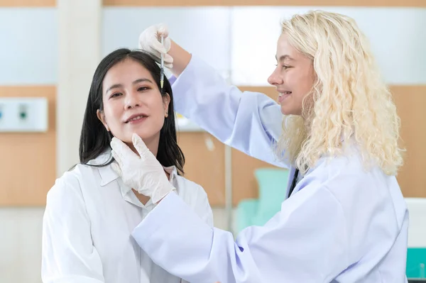 Woman doctor cosmetologist injects a filler into the cheek of the patient's woman. Cosmetology concept