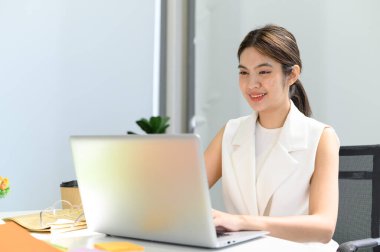 İş kadını ofiste dizüstü bilgisayarla uğraşırken masada oturuyor. Belge yazan, e-postaları kontrol eden ve işyerindeki çevrimiçi toplantılara katılan kadınlar
