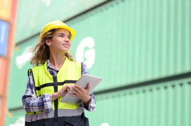 Engineer women wear yellow helmets and reflection shirts working on tablet computers to check inventory details of containers box. Inspector or Safety Supervisor in Container Terminal