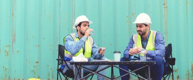 İki lojistik çalışanı mola sırasında nakliye konteynırında oturup konuşuyorlar ve dinleniyorlar. Kargo gemisi ithalat fabrikası lojistik ulaşım ve küresel iş konsepti