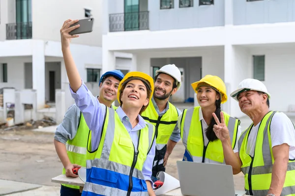 Happy engineers and formats, male and female colleagues in safety vests with helmets taking selfies at under-construction building sites. teamwork