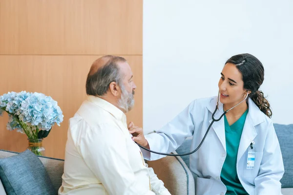 stock image Young female doctor in white medical coat attending physician using stethoscope listening an old patient for checking heartbeat. Medicine and health care concept. cardiology concept