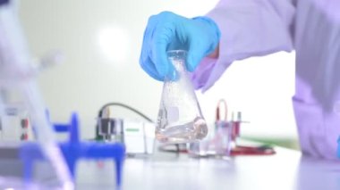 Plastik eldiven giymiş kimyager laboratuvar şişesini sallıyor. Tıp ve Biyoteknoloji Araştırmacıları için Bilimsel Laboratuvar.