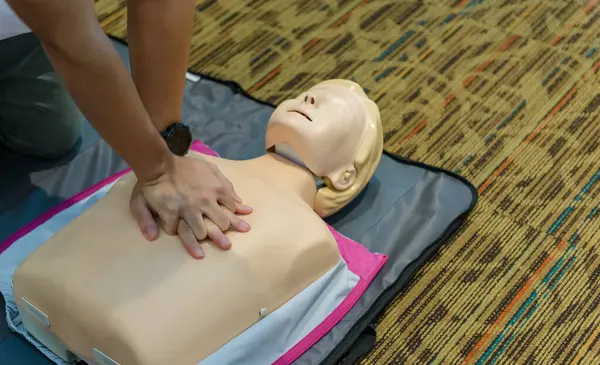 CPR First Aid Training with CPR dummy in the class. Demonstrating chest compressions concept
