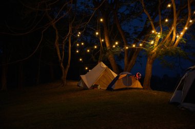 Çim avlusunda kamp çadırı ve koyu mavi gökyüzünün altında sıcak gece ışığı. Tatilde aile pikniği