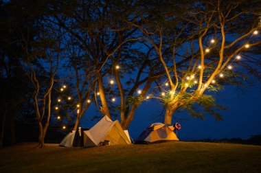 Çim avlusunda kamp çadırı ve koyu mavi gökyüzünün altında sıcak gece ışığı. Tatilde aile pikniği