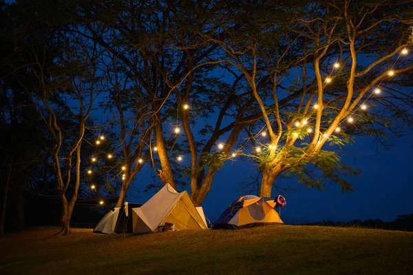 Çim avlusunda kamp çadırı ve koyu mavi gökyüzünün altında sıcak gece ışığı. Tatilde aile pikniği