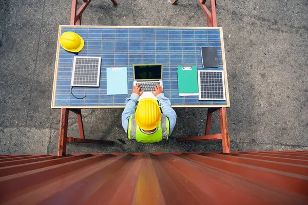 stock image Top view of engineer wearing white helmets and safety vests use laptop computer to check solar photovoltaic panels for new project. green alternative energy concept