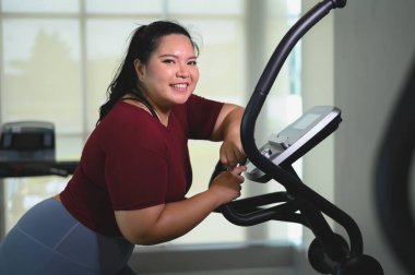 Spor salonunda eliptik antrenör üzerinde egzersiz yapan Asyalı şişman genç kadınların portresi. Kilo verme egzersizi, sağlıklı yaşam tarzı konsepti