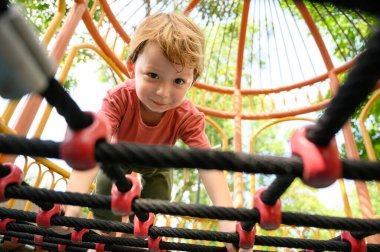 Okul bahçesinde kaftanlara tırmanan şirin bir çocuk. Mutlu ve macera dolu sporların tadını çıkarın.