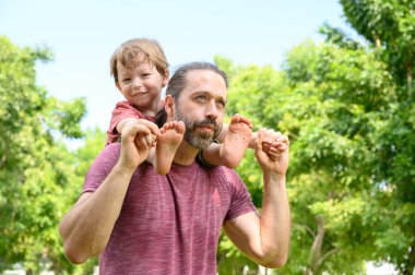 Küçük çocuk yaz günü babasıyla oynuyor. Baba parkta oğlunu omuzlarında taşır. Baba günü mutlu aile çocuğu rüyası konsepti