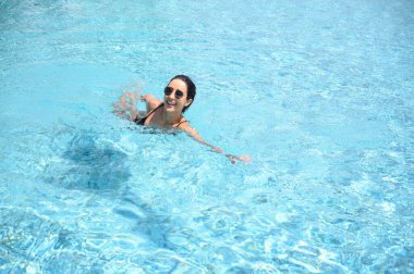 Havuzda güneş gözlüklü, bikinili, gülümseyen genç bir kadın. Yazın dinlenen güzel bir dişi. Yaz tatili konsepti