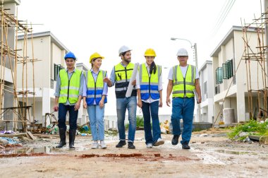 İnşaat sahasında kasklı güvenlik yelekleri giyen bir grup mutlu müteahhit, mühendis ve format duruyor. takım çalışması konsepti
