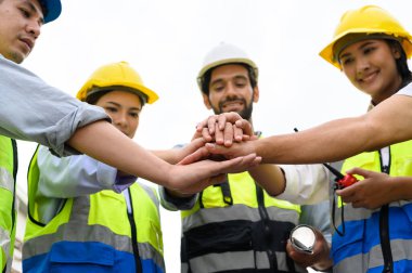 Group of contractors, engineers and formats in safety vests with helmets join hands to work together to successfully complete a construction project on construction site. cooperation and success concept