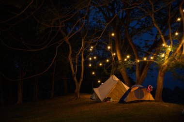 Çim avlusunda kamp çadırı ve koyu mavi gökyüzünün altında sıcak gece ışığı. Tatilde aile pikniği