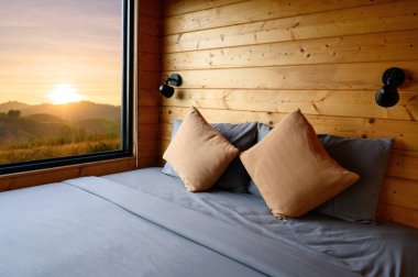 Pencerede yaz günbatımında rahat yataklı ahşap kulübenin içi.