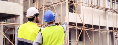 Banner of Construction engineer and architect check plan working with the blueprint on construction site. They are in safety vests with helmets for safety. Back view of the Construction project concept. 
