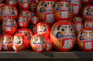 Japonya 'nın Minoh, Osaka kentindeki Katsuo-ji tapınağındaki ahşap rafta yığınla kırmızı Daruma bebeği var. Kanji İngilizceye çevrildi: 