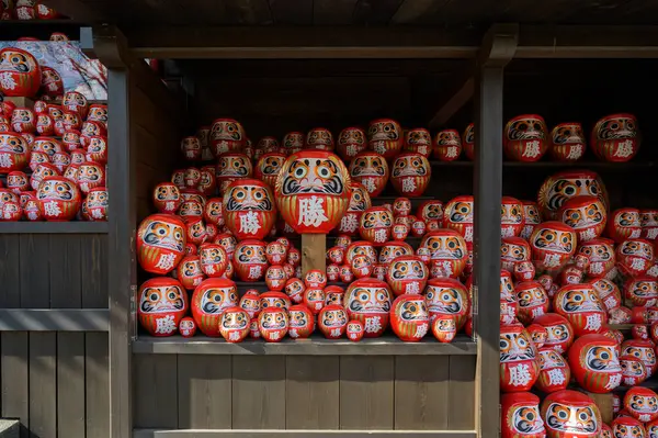 Japonya 'nın Minoh, Osaka kentindeki Katsuo-ji tapınağındaki ahşap rafta yığınla kırmızı Daruma bebeği var. Kanji İngilizceye çevrildi: 
