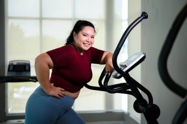 Spor salonunda eliptik antrenör üzerinde egzersiz yapan Asyalı şişman genç kadınların portresi. Kilo verme egzersizi, sağlıklı yaşam tarzı konsepti