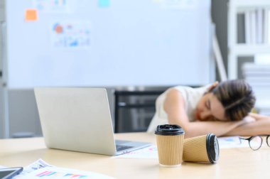 Masada iki kahve kâğıdı fincanı ve arka planda uyuyan Asyalı bir kadın. Fazla mesai konsepti. Kağıt bardağa odaklanmayı seç