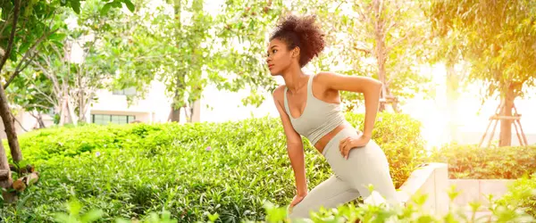 Açık hava parkında uzayan genç bir kadının portresi. Güzel Afrikalı kadın hazırlık, antrenman, spor, yaşam tarzı, yaz havası konsepti