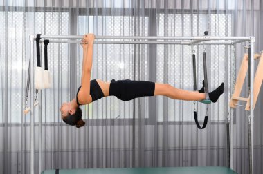 Spor kadını spor salonunda esnek olmak ve vücut geliştirme eğitimi almak için trapez masasında pilates yapıyor.