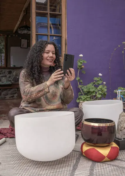 Tibet şarkı kaseleriyle meditasyon yaparken elinde telefon tutan ve gülümseyen bir kadın.