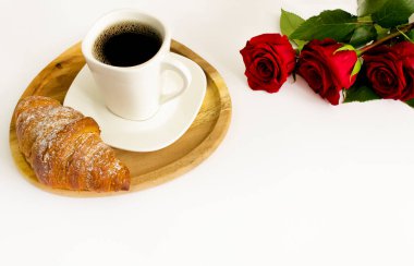 Holiday breakfast for St. Valentine A cup of coffee with a croissant and a bouquet of roses on a white background. Copy space.