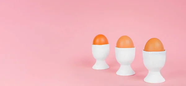 Eggs in an egg cups on a pink background. Preparation and celebration of Easter. Copy space.