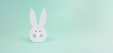 Minimalist Paskalya kompozisyonu. Turkuaz arka planda beyaz dekoratif tavşan. Boşluğu kopyala.