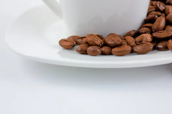 ソーサーの上のコーヒー豆が閉じます 白いテーブルの上にコーヒーを一杯 — ストック写真