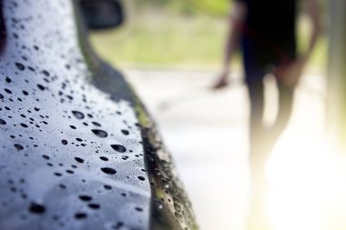 Bir adam arabasını yüksek basınçlı su altında yıkar. Temassız self servis lavabosu..