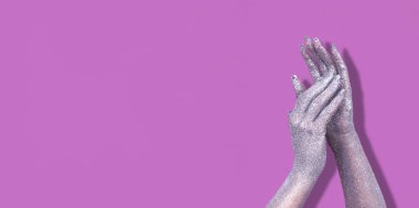 Işıldayan gümüş eller ışığı parlak mor bir zemin üzerinde yansıtıyor, yaratıcılık sergiliyor..