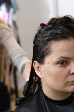 Kuaför koltuğunda oturan bir kadın saçını bir kuaföre yaptırıyor..