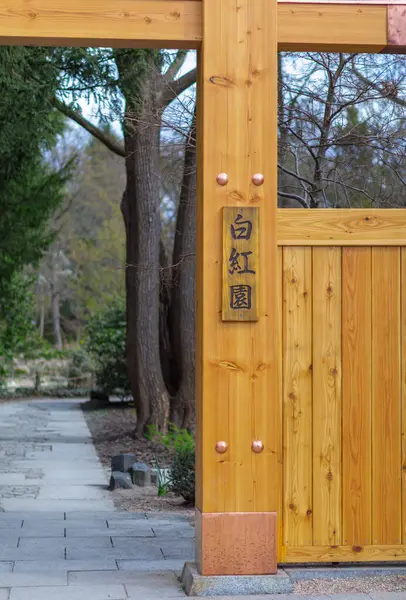 Tahta bir kapı, sakin bir Japon bahçesinin girişini işaret ediyor..