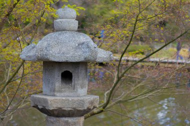 Bir Japon bahçesindeki sakin bir göletin yanında taş bir fener duruyor..
