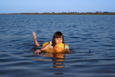 Bir çocuk yüzme cihazı takarken sakin bir gölde nazikçe kürek çeker..