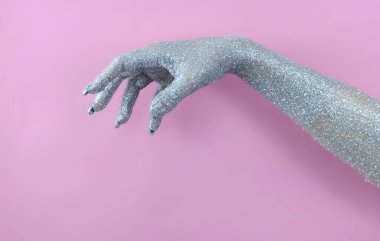 Işıl ışıl gümüş bir el öne doğru uzanır, yumuşak pembe bir arka planda parlak bir parıltı sergiler..