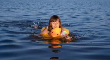 Çocuk turuncu ördek yüzerken durgun suda kürek çekiyor..
