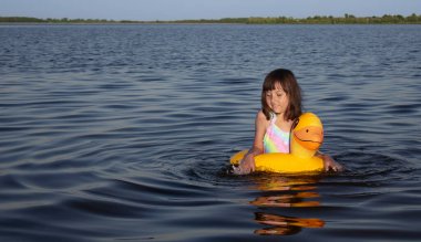 Genç bir kız dingin bir gölde parlak sarı bir ördeğin üzerinde oynuyor..