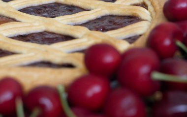 Kafes kenarlı vişneli turta, ahşap bir yüzeyde taze kirazların yanında oturur..